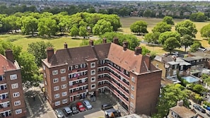 A multi-story residential building with a brick facade, multiple balconies, and a parking area with several cars. - 2BDR 2BA Peckham Rye Flat with Park Access (Greater London)