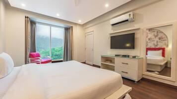 Habitación de hotel con una cama grande, un escritorio con televisión de pantalla plana, armario y puerta corredera que da a un balcón con vistas a la vegetación.