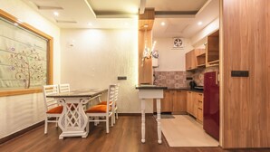 A modern kitchen with wooden cabinets, a dining table with chairs, and a ceiling fan. - Aloha On The Ganga Almost Heaven 2BR Condo With Pool (Rishikesh)