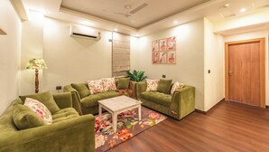 A living room with a sofa set, a coffee table, a wall-mounted air conditioner, and a door. - Aloha On The Ganga Almost Heaven 2BR Condo With Pool (Rishikesh)
