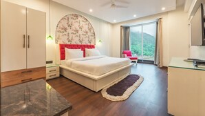 A modern bedroom with a bed, wardrobe, bedside tables, a desk, and a view of greenery outside. - Aloha On The Ganga Almost Heaven 2BR Condo With Pool (Rishikesh)