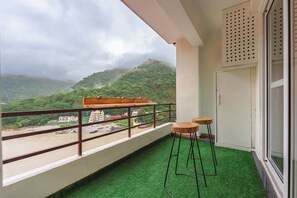 A balcony with artificial grass, a wooden bench, and two stools.