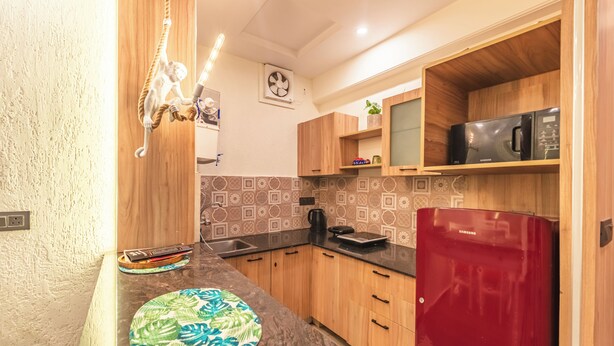 A compact kitchen with wooden cabinets, a red refrigerator, a microwave, and a coffee maker. - Aloha On The Ganga Almost Heaven 2BR Condo With Pool (Rishikesh)