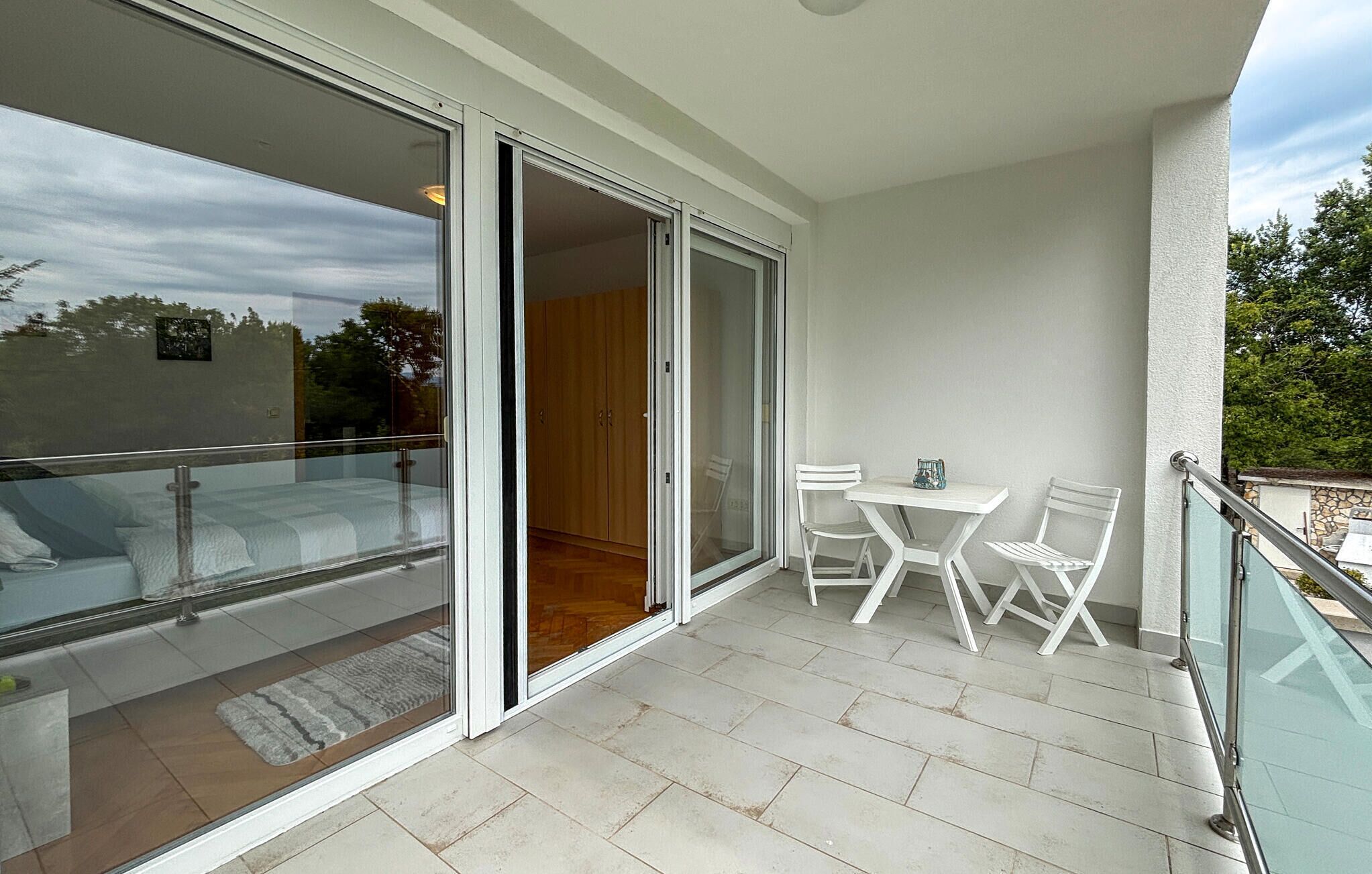 A balcony with a glass door leading to a bedroom, a small table with chairs, and a view of the outdoors.