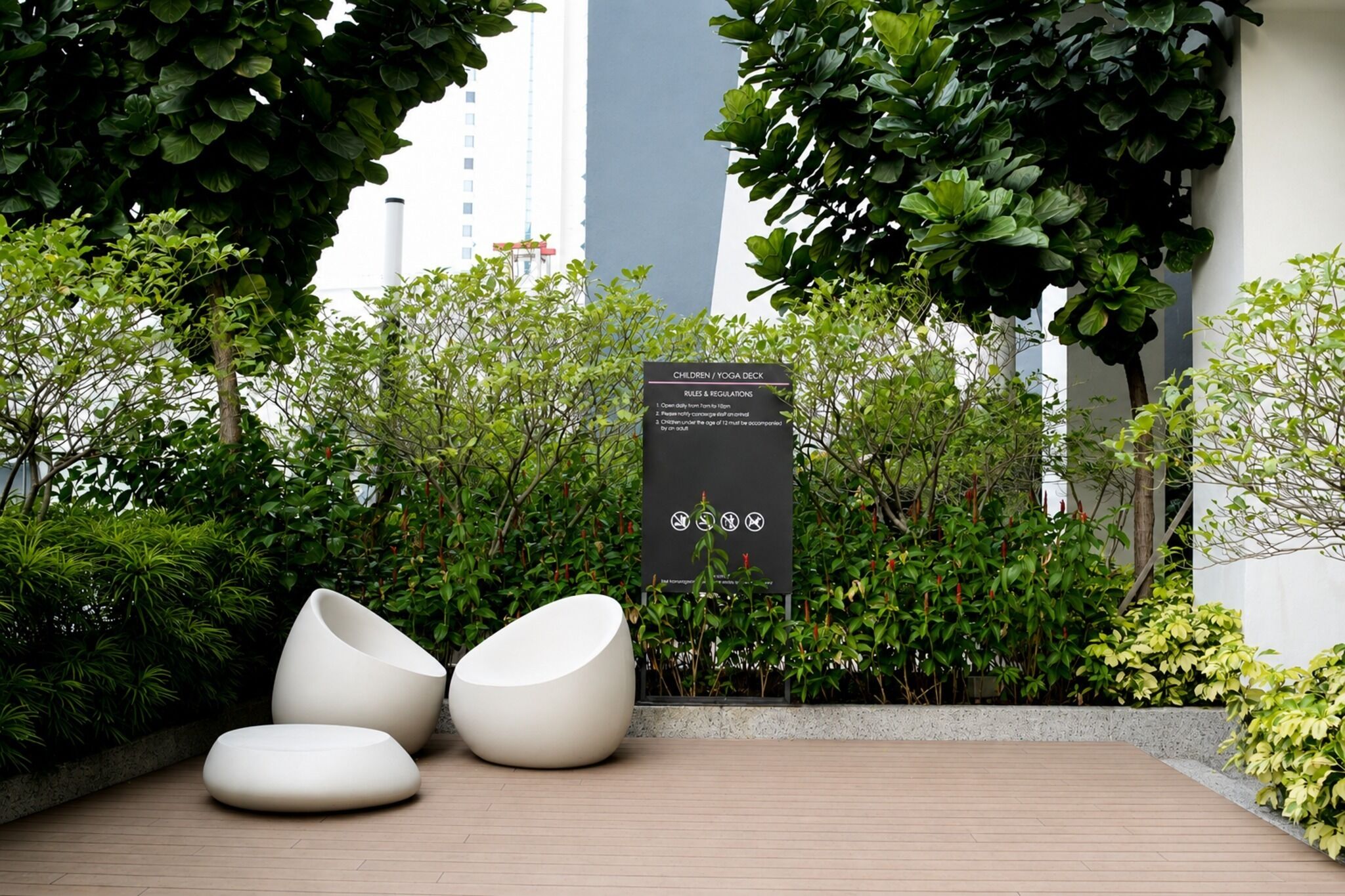 Een terras met moderne witte stoelen, omringd door weelderige begroeiing en een bord met regels voor een kinder-/yogadek.