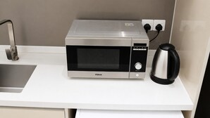 A microwave oven with a digital display, a kettle, and a power outlet on a white countertop. - Quill Residences KLCC by Moonlight (Kuala Lumpur)
