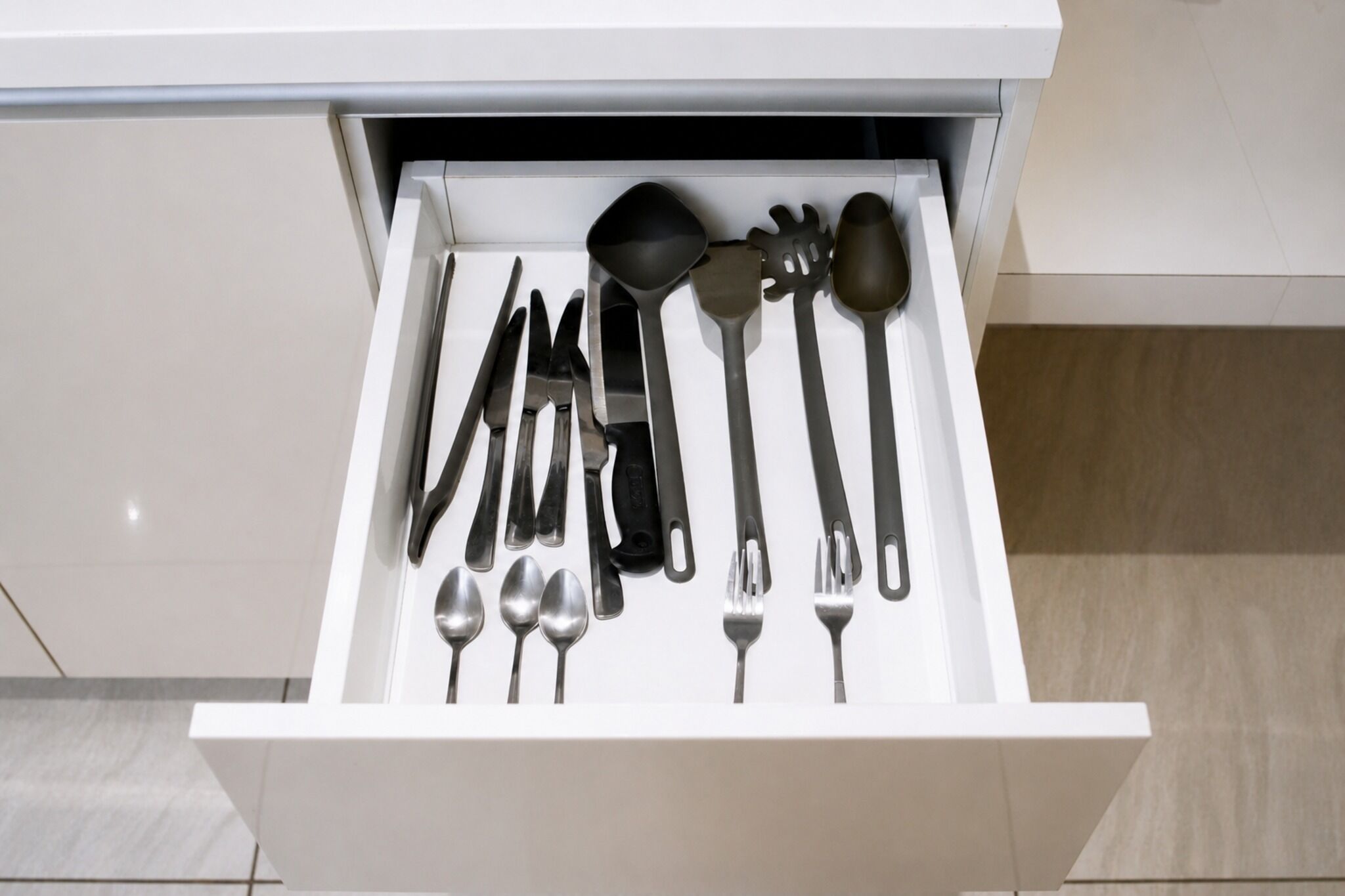 A drawer containing various kitchen utensils including spoons, forks, knives, and a ladle.
