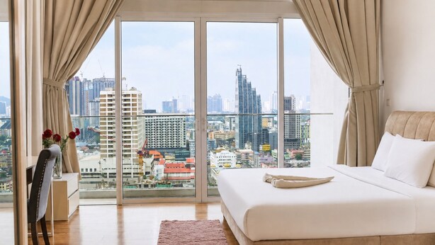 A bedroom with a large bed, a desk, and a chair, with a city view through floor-to-ceiling windows. - Quill Residences KLCC by Moonlight (Kuala Lumpur)