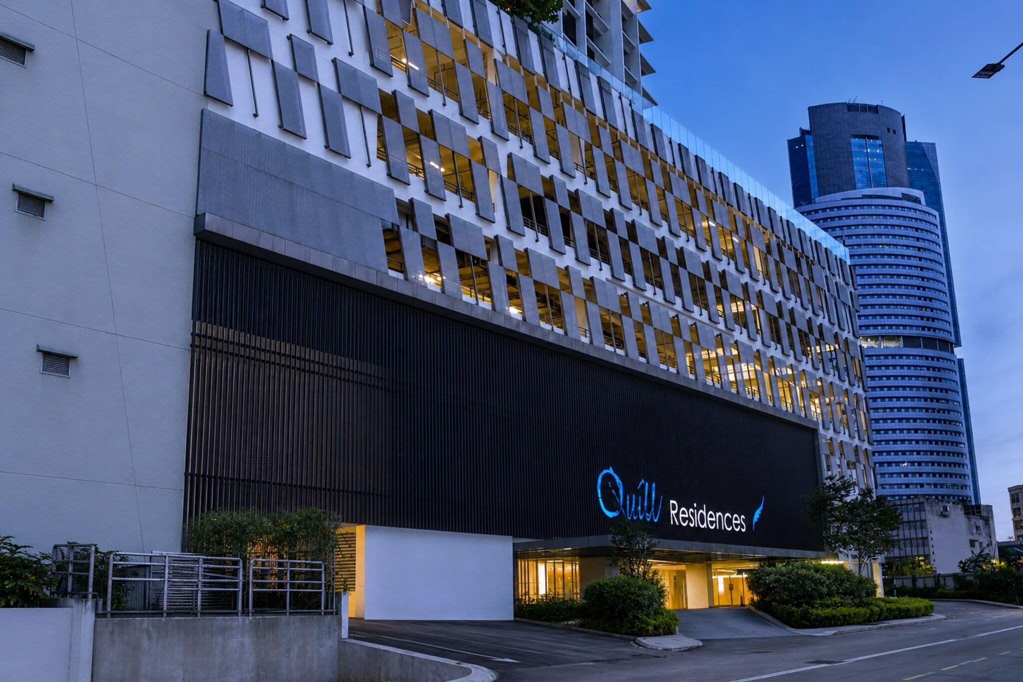 A modern building with a large illuminated sign for 'Quill Residences'.