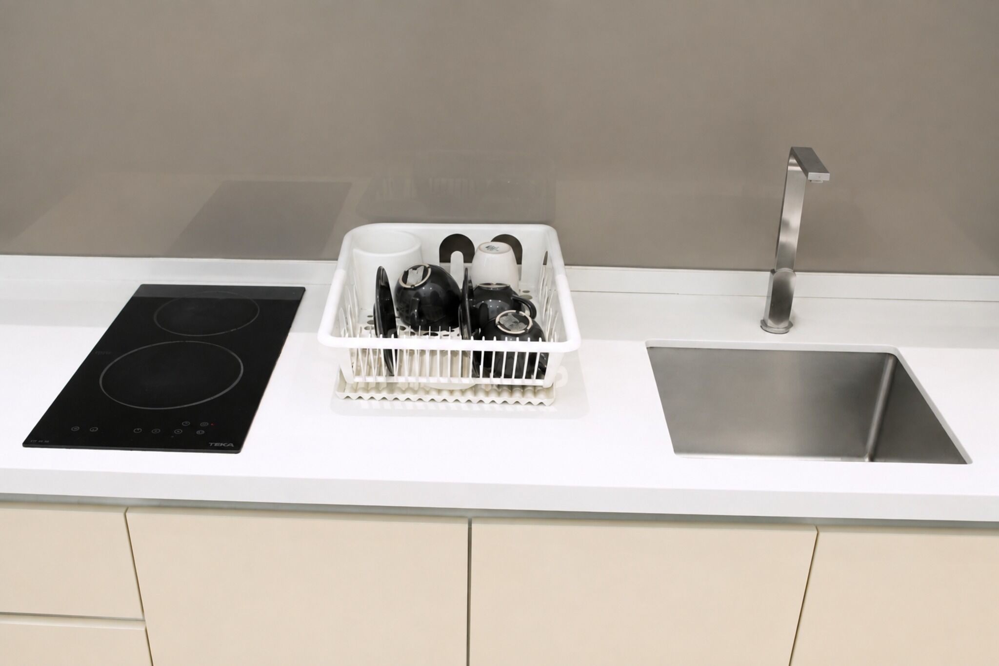 Une cuisine dotée d’une plaque de cuisson à induction noire, d’un évier blanc et d’un égouttoir à vaisselle.