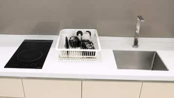 Una cocina con una placa de inducción negra, un lavabo blanco y un escurreplatos.