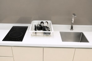 A kitchen with a black induction cooktop, a white sink, and a dish drying rack. - Quill Residences KLCC by Moonlight (Kuala Lumpur)