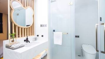 Un baño moderno con un tocador blanco, un espejo grande, cabina de ducha con mampara de cristal y un inodoro.
