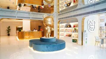 Um lobby de hotel moderno com um balcão de recepção, uma escultura dourada única e um átrio com vários níveis e lojas.