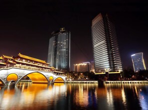 A night view of a cityscape with modern high-rise buildings and a traditional bridge with illuminated arches. - Chengdu Ben Hotel (Chengdu)
