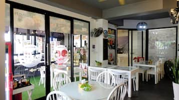 Interior de restaurante com mesas e cadeiras brancas, um ventilador de teto e um painel de vidro com cardápios.