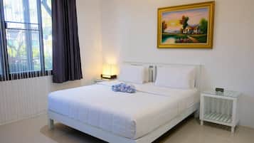 Quarto de hotel com uma cama grande, uma mesa de cabeceira com abajur, um quadro na parede e uma janela com cortinas.