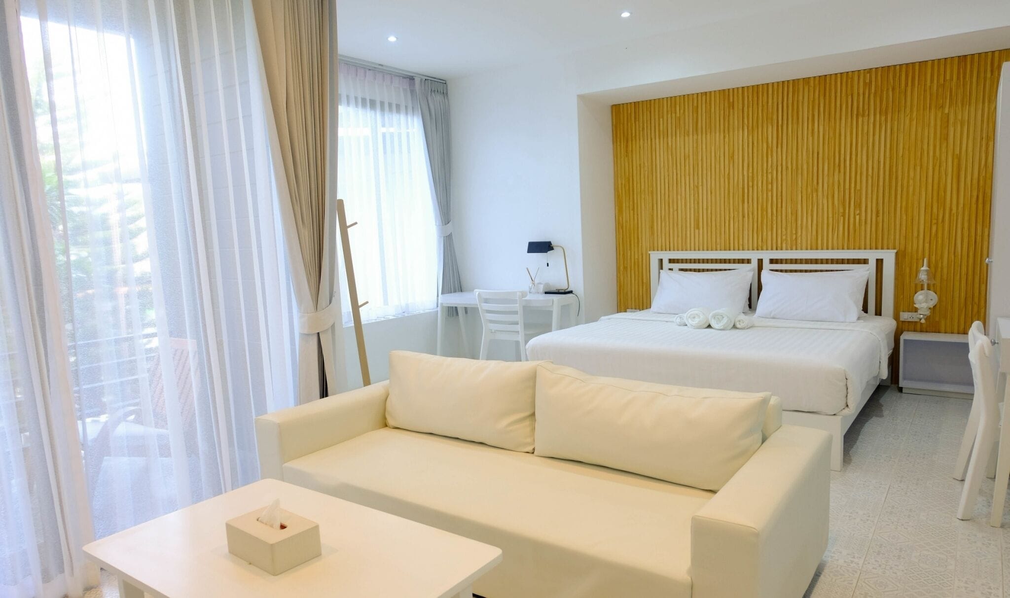 A hotel room with a bed, a sofa, a desk, and a window with curtains.