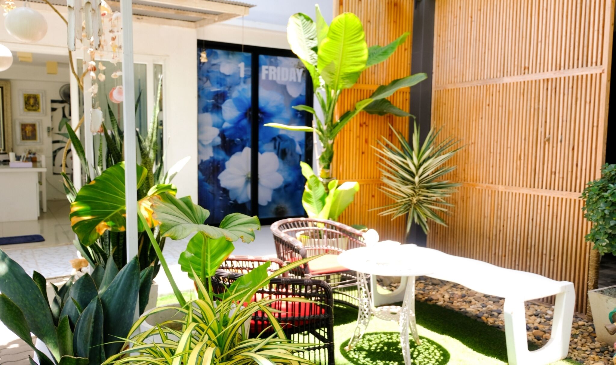 A well-maintained outdoor area with a variety of plants, a white table, and wicker chairs.