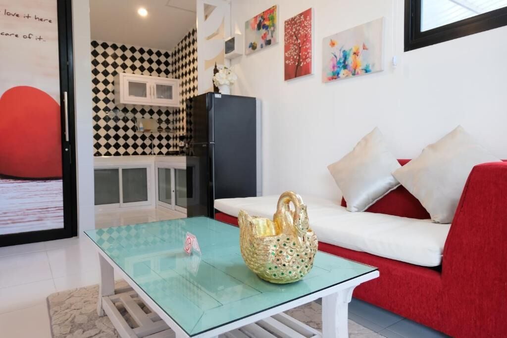 A modern living room with a glass coffee table, a red sofa, and a kitchen area with a black refrigerator.