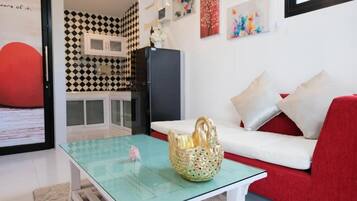 A modern living room with a glass coffee table, a red sofa, and a kitchen area with a black refrigerator.