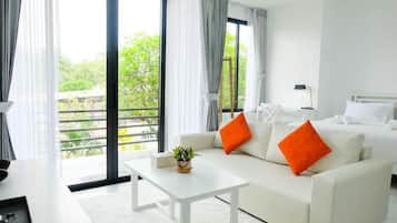 Quarto de hotel moderno com sofá branco, uma mesa pequena e uma cama com roupa de cama branca.