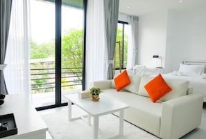 Quarto de hotel moderno com sofá branco, uma mesa pequena e uma cama com roupa de cama branca.