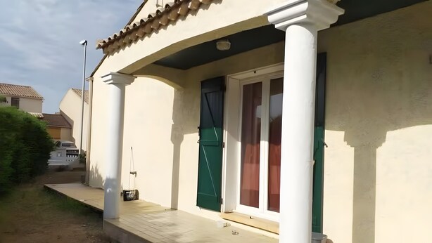 Un edificio residenziale con un portico coperto, una porta con persiana verde e un piccolo gradino che conduce all'ingresso.