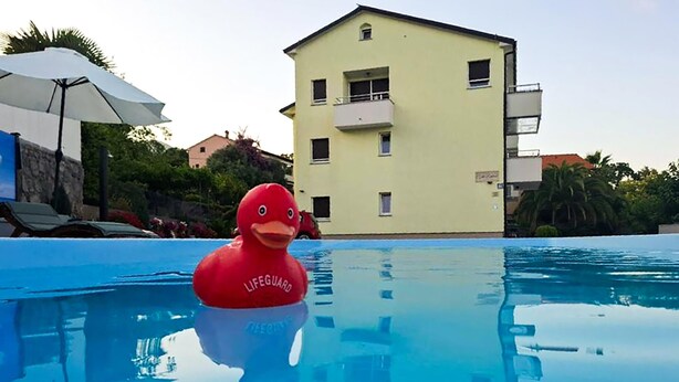 Eine rote Schwimmenten in einem Pool, im Hintergrund ein Gebäude.