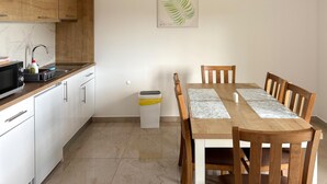 Eine moderne Küche mit Holzausstattung, einer Mikrowelle und einem Spülbecken. Ein Esstisch mit Stühlen und einem Mülleimer sind ebenfalls vorhanden.
