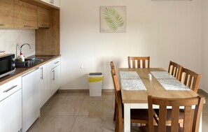 A modern kitchen with wooden cabinets, a microwave, and a sink. There's a dining table with chairs and a trash bin. - Lovely apartment in Opric with swimming pool (Opric)