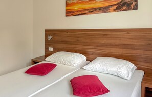 A double bed with white linens and two red pillows, a wooden headboard, a nightstand with a lamp, and a painting of a sunset on the wall. - Lovely apartment in Opric with swimming pool (Opric)