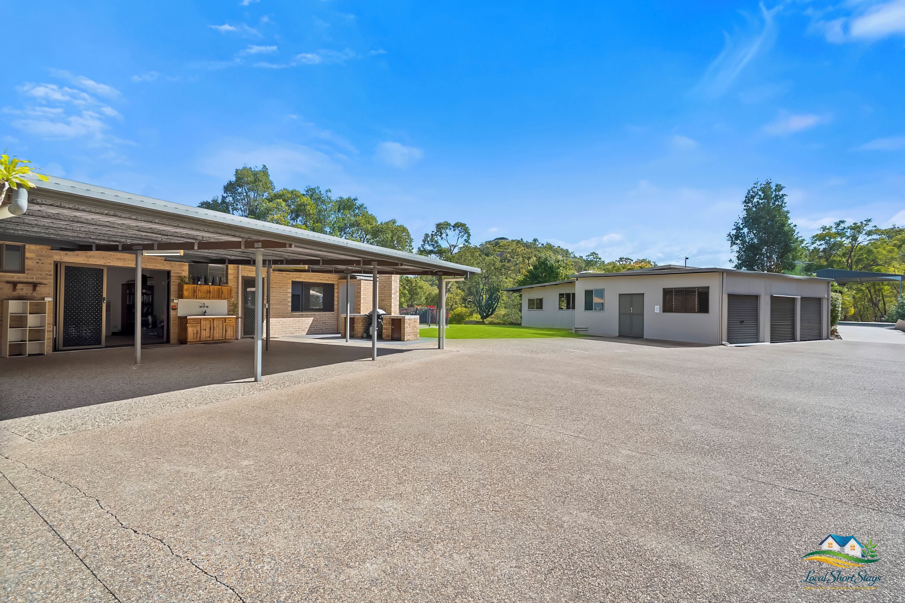 A building with a covered outdoor area, a small adjacent structure, and a paved driveway.
