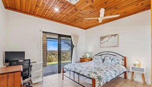 A bedroom with a bed, a TV, a desk, and a window with a view.