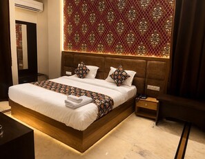 A modern hotel room with a large bed, a bedside table, a nightstand, and a decorative wall panel. - Hotel Sukh By Mehar Group (Jaipur)
