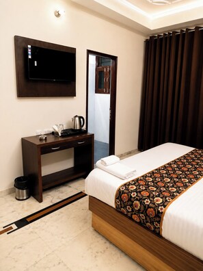 Ein Hotelzimmer mit Bett, Schreibtisch mit Wasserkocher, Wandfernseher und Spiegel.