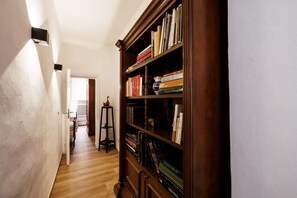Ein Flur mit einem Bücherregal aus Holz, voll mit Büchern, einem kleinen Hocker und einer Tür, die in einen anderen Raum führt.