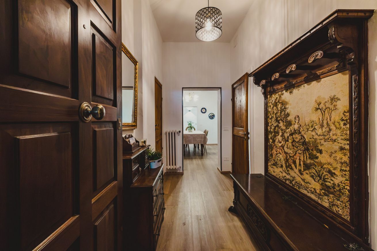 A hallway with wooden doors, a radiator, a dining area in the background, and a large framed painting on the wall.