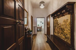A hallway with wooden doors, a radiator, a dining area in the background, and a large framed painting on the wall. - GuestHost - Dimora Camollia in the Heart of Siena (Siena)
