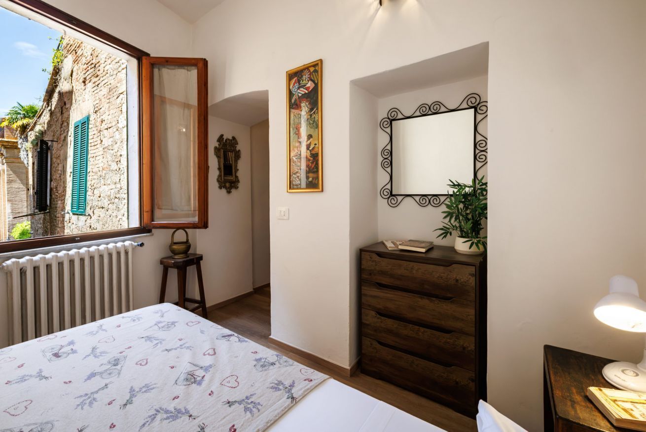 A bedroom with a bed, a dresser, a mirror, a radiator, and a window with shutters.