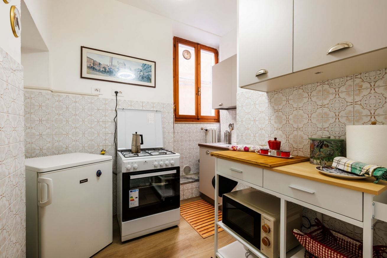 A compact kitchen with a refrigerator, stove, oven, and a wooden countertop with kitchenware.