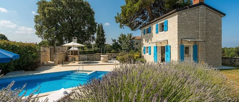A stone building with blue shutters, a swimming pool, and a garden with lavender.