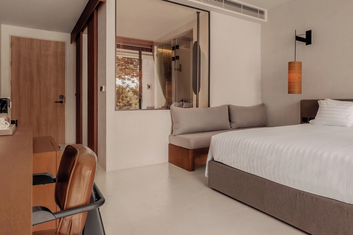 A modern bedroom with a large bed, bedside tables, a seating area, and a mirror.