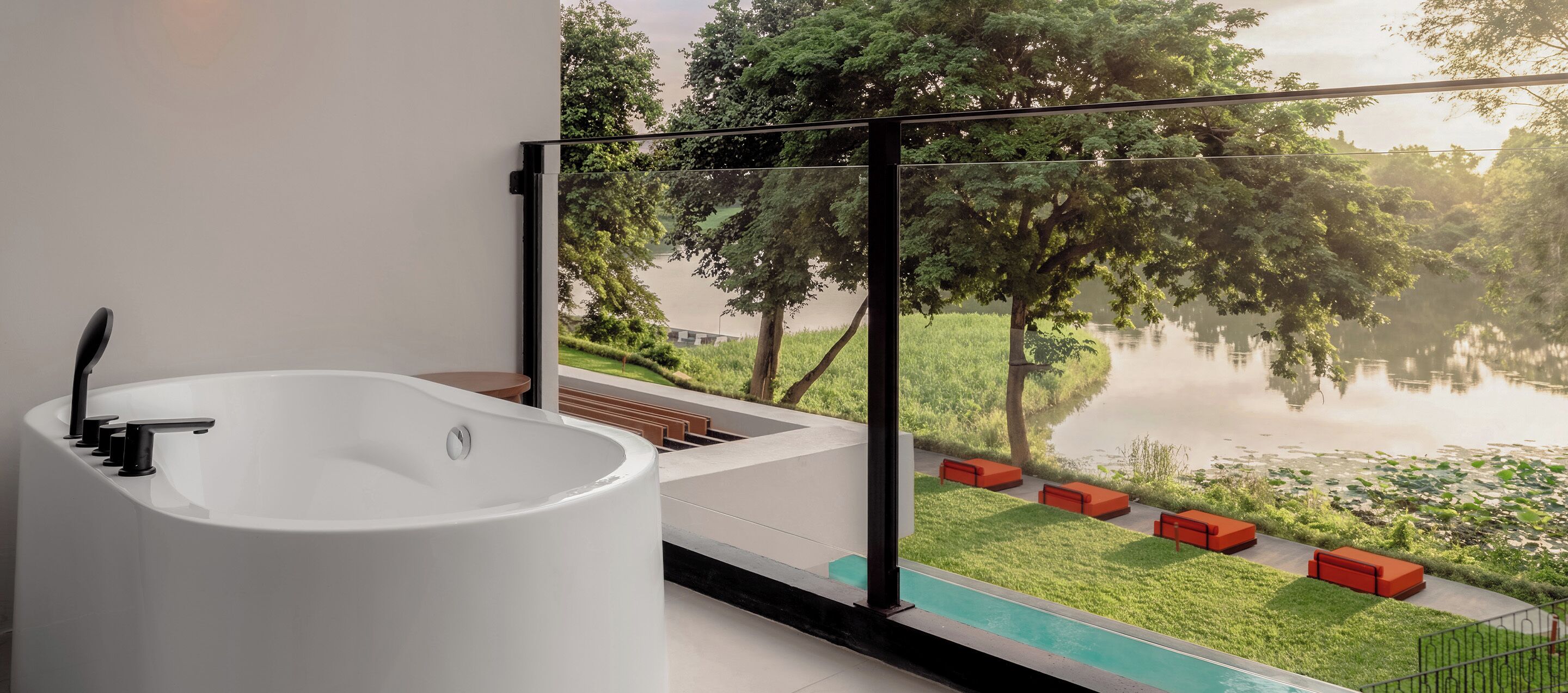 Ein modernes Badezimmer mit einer freistehenden Badewanne, einem großen Fenster mit Blick auf einen See und viel Grün.