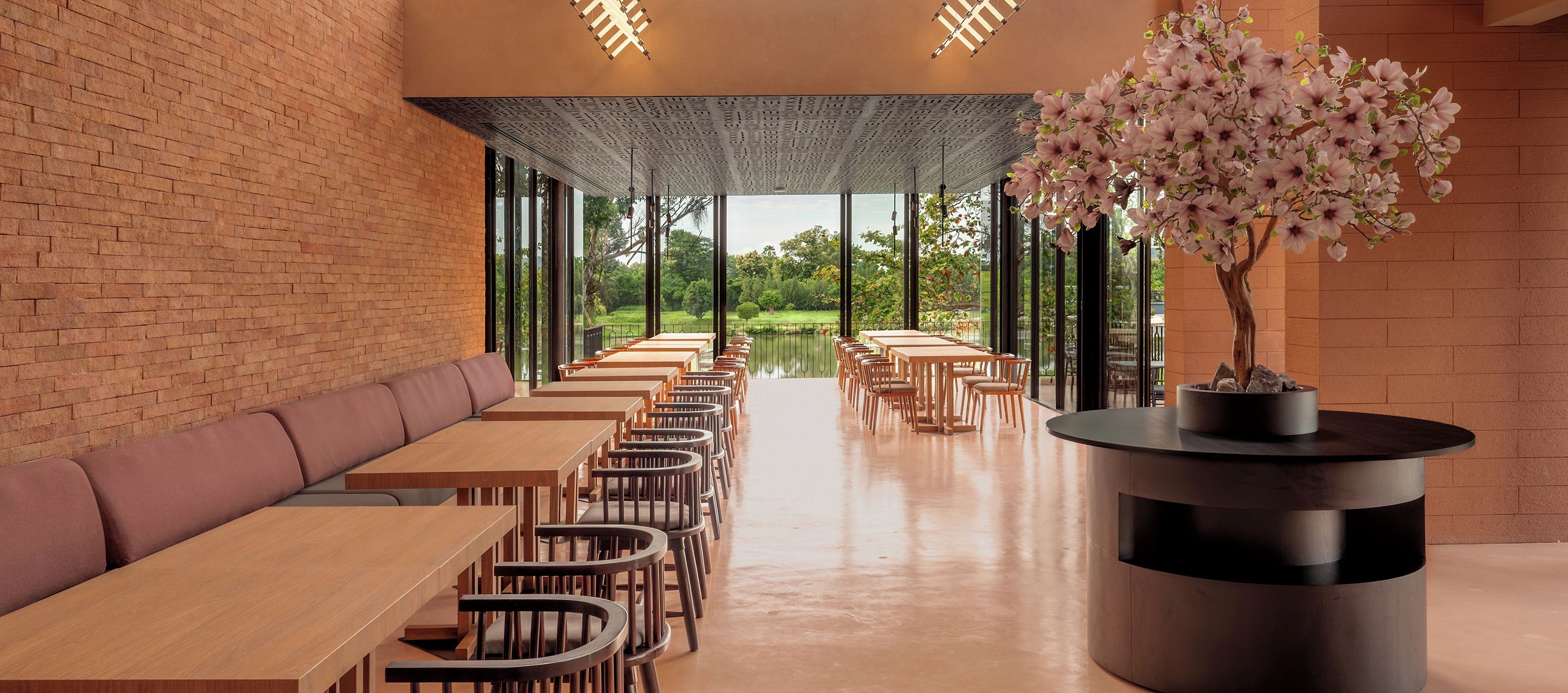 A restaurant with a brick wall, wooden tables and chairs, a bench, and a bonsai tree.