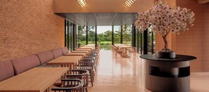A restaurant with a brick wall, wooden tables and chairs, a bench, and a bonsai tree.