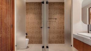 A modern bathroom with a wooden door, a glass shower enclosure, and a vanity with a mirror. - Hykyo River Kwai Hotel (Kanchanaburi)