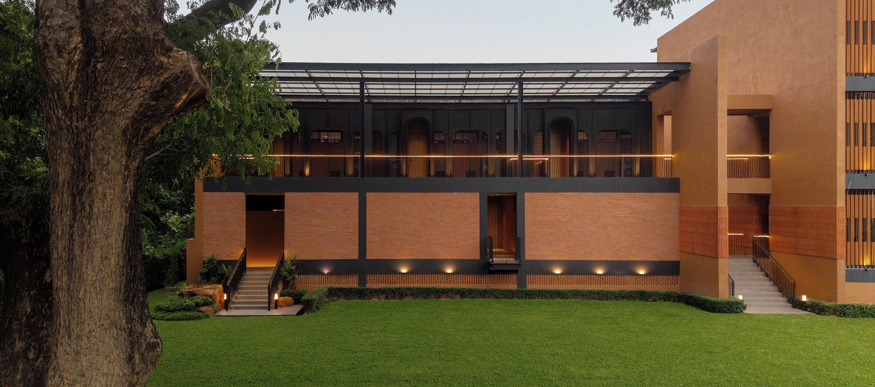 A modern building with a flat roof, multiple levels, and a covered outdoor area with a staircase leading to an upper level.