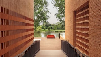 Un pasillo con piso de madera que conduce a una terraza de madera con vista a una masa de agua, con un banco rojo y barandillas de metal.