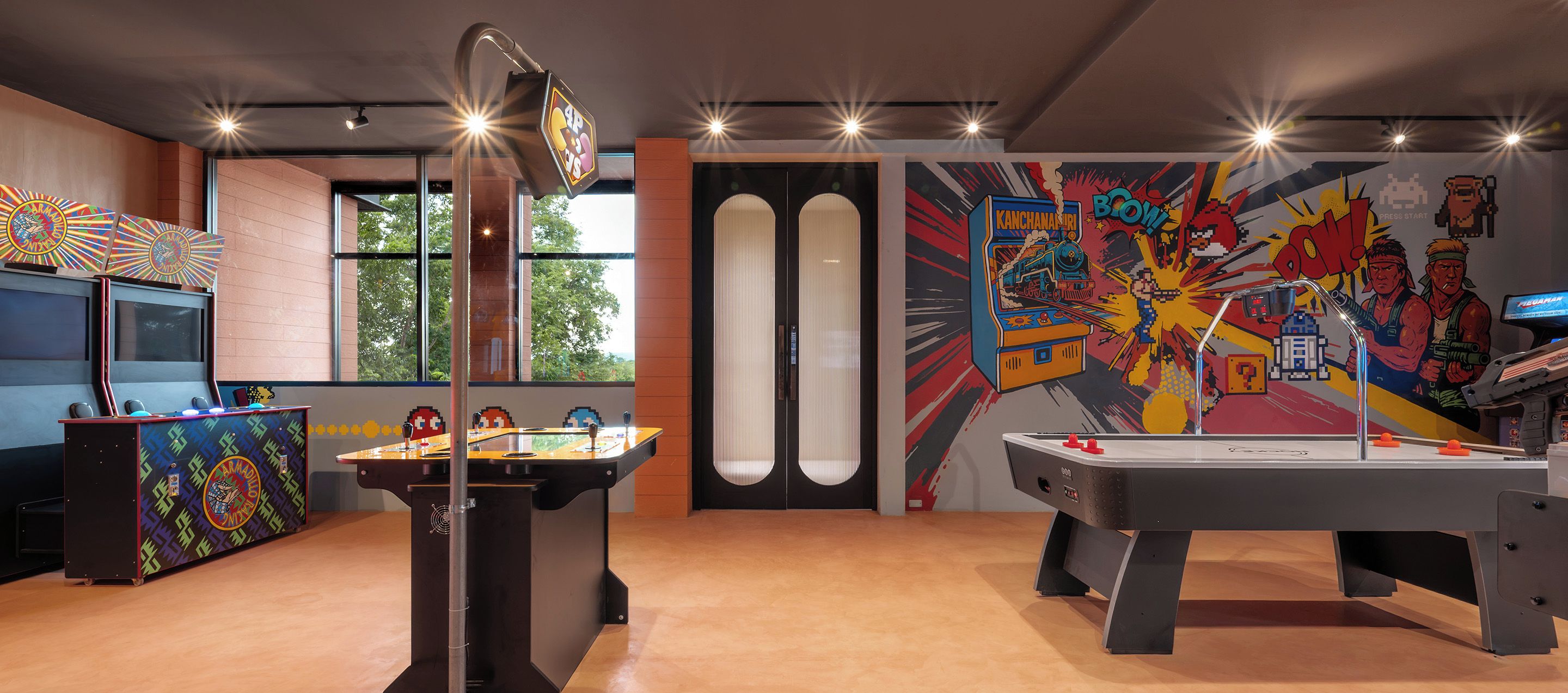 Une pièce équipée de deux tables de baby-foot, d’un jeu de fléchettes et ornée d’une fresque murale colorée.